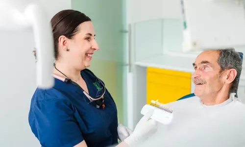 Zahnärztin berät einen Patienten zur Zahnfarbe mit einem Farbmuster, ästhetische Zahnheilkunde in Dornbirn